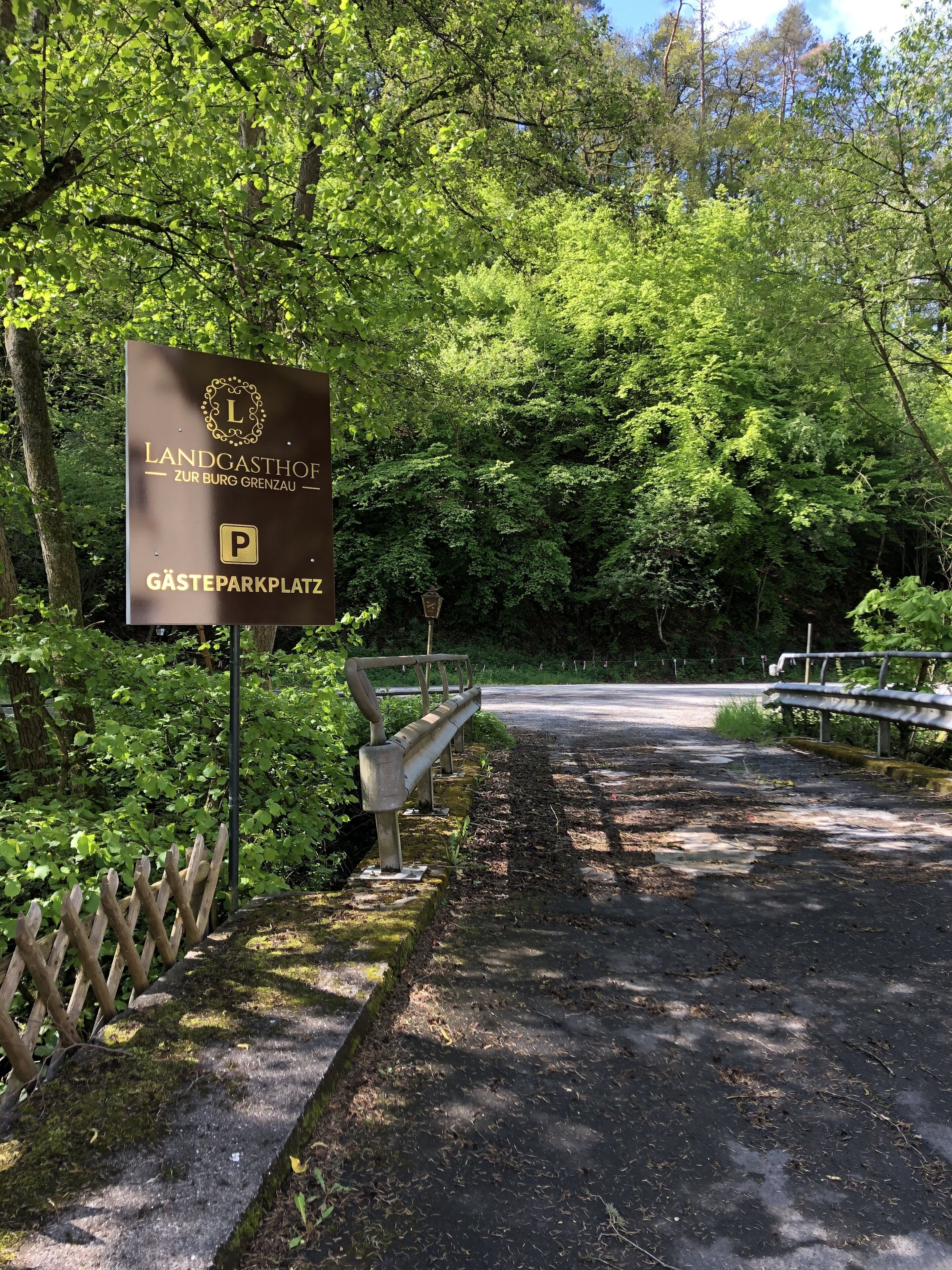 A sign for Landgasthof Zur Burg Grenzau with a parking symbol, surrounded by lush greenery.