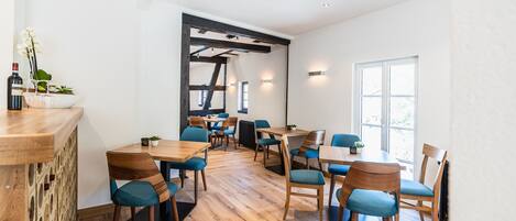 A modern dining area with wooden tables and chairs, a bar counter, and a large window providing natural light.