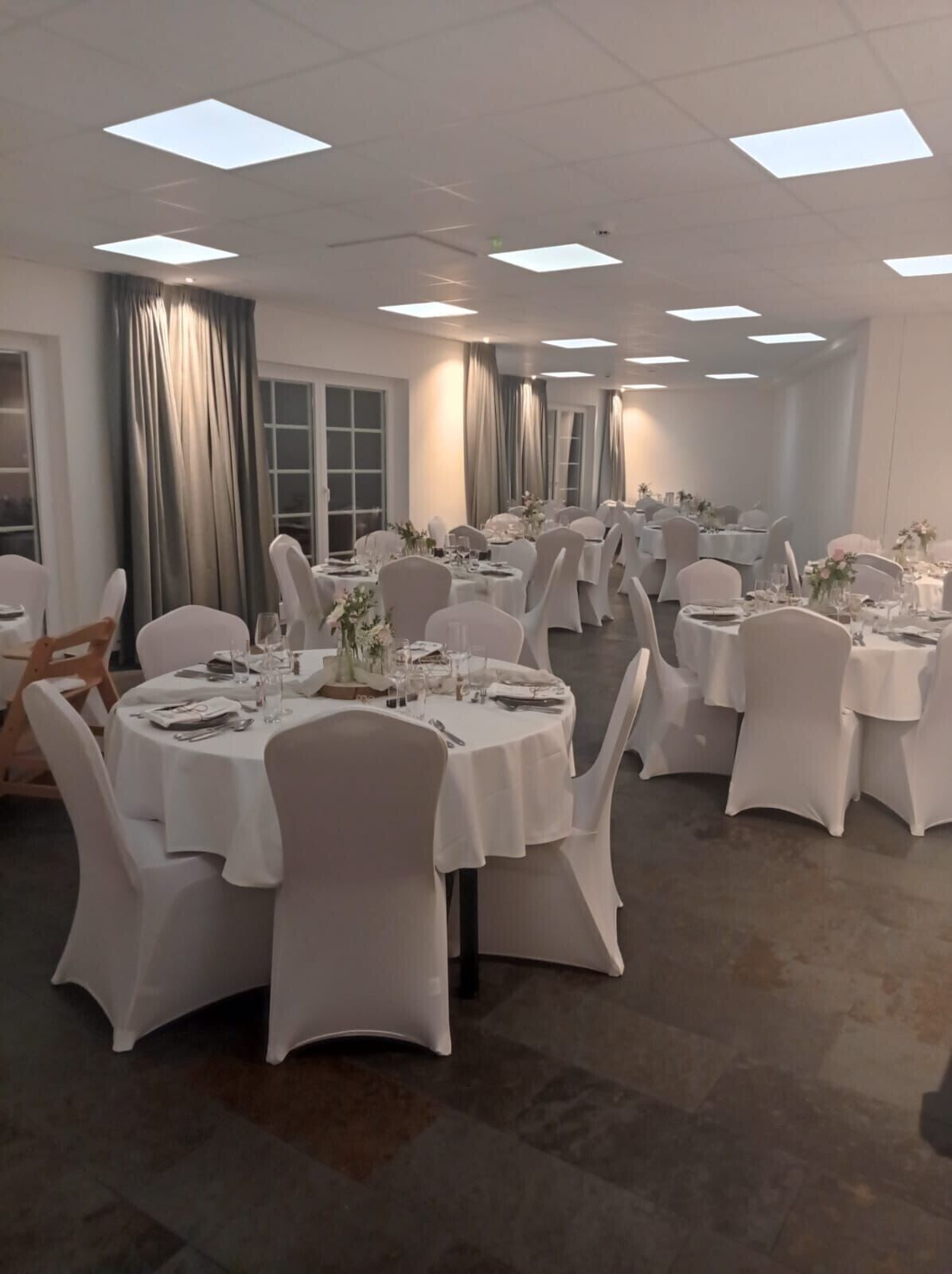 Une salle de banquet avec des tables rondes, des nappes blanches et des chaises.