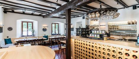 Un restaurante con vigas de madera a la vista, una estantería para vinos y una zona de bar con estantes llenos de copas y botellas.