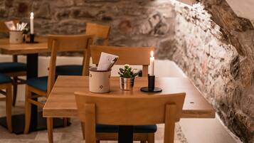 Un rincón comedor acogedor con mesas y sillas de madera, una vela y una planta pequeña sobre una mesa.