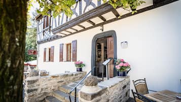 Un bâtiment traditionnel avec un escalier en pierre menant à une porte en bois, des pots de fleurs et une table avec des chaises à l’extérieur.