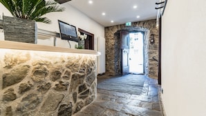 A stone-walled reception area with a reception desk, a mounted TV, and a potted plant. - Landgasthof zur Burg Grenzau (Hoehr-Grenzhausen)
