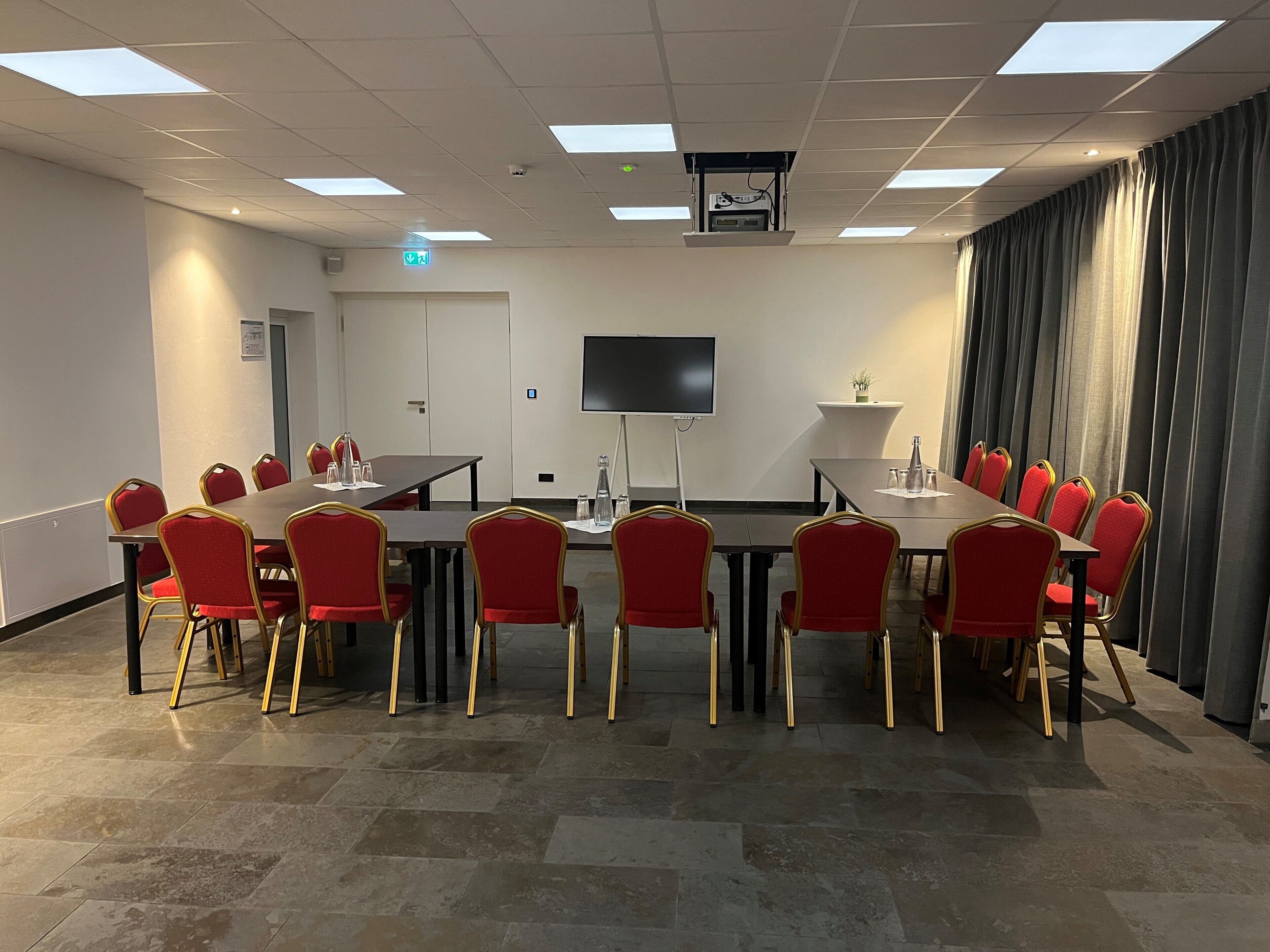 Une salle de conférence équipée d’une grande table, de chaises rouges, d’un téléviseur à écran plat et d’un projecteur.
