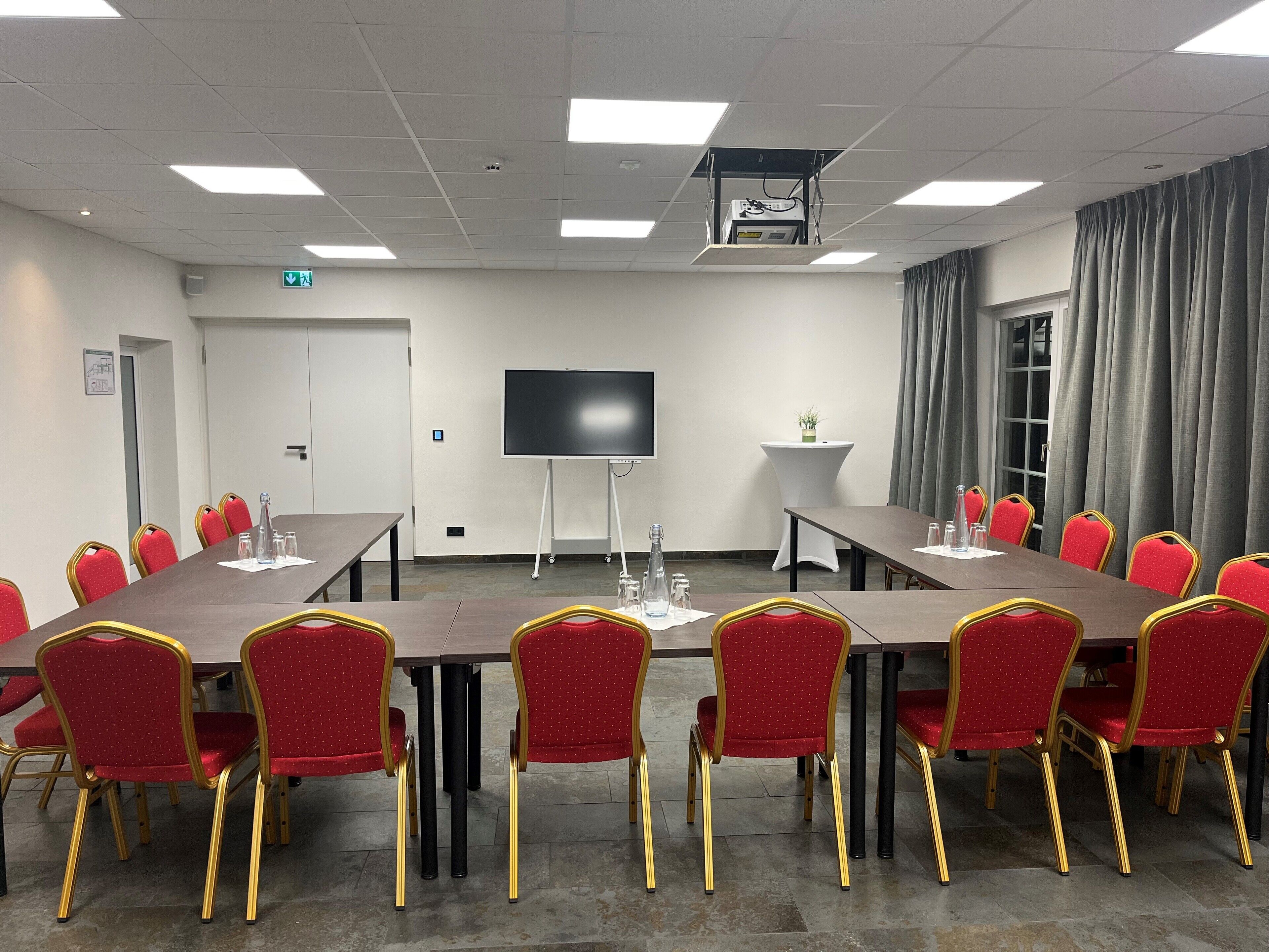 A conference room with a long table, red chairs with gold accents, a flat-screen TV, and a small side table with a plant.