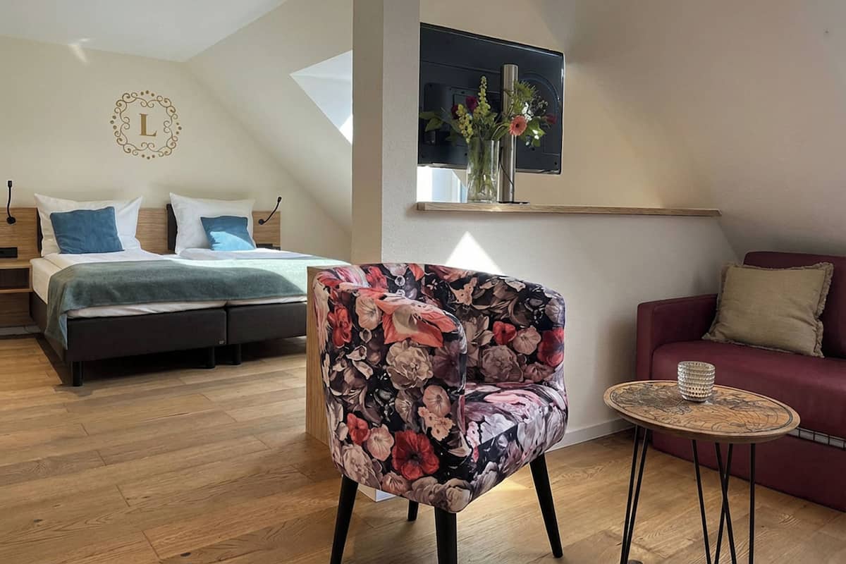 Une chambre à coucher avec un lit, un fauteuil à motifs floraux, un canapé rouge et une petite table ronde.
