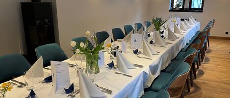 A long dining table set with white tablecloths, teal chairs, and floral centerpieces.