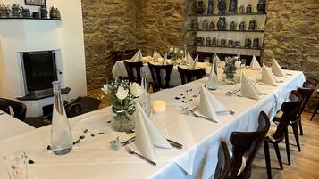 A long dining table set with white tablecloths, silverware, and glassware, surrounded by wooden chairs.