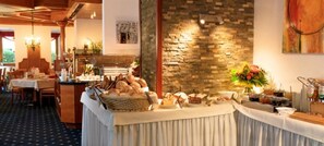 Disposição de buffet com diversos alimentos e um fundo de parede de pedra.