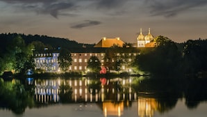 A nighttime view of a historic building with a large reflective lake in front. - Kloster Seeon (Seeon-Seebruck)