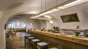 A bar area with wooden counter and stools, a chalkboard menu, and a view of the dining area with tables and chairs. - Kloster Seeon (Seeon-Seebruck)