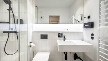 A modern bathroom with a glass shower enclosure, a white toilet, a sink with a mirror, and a towel rack.