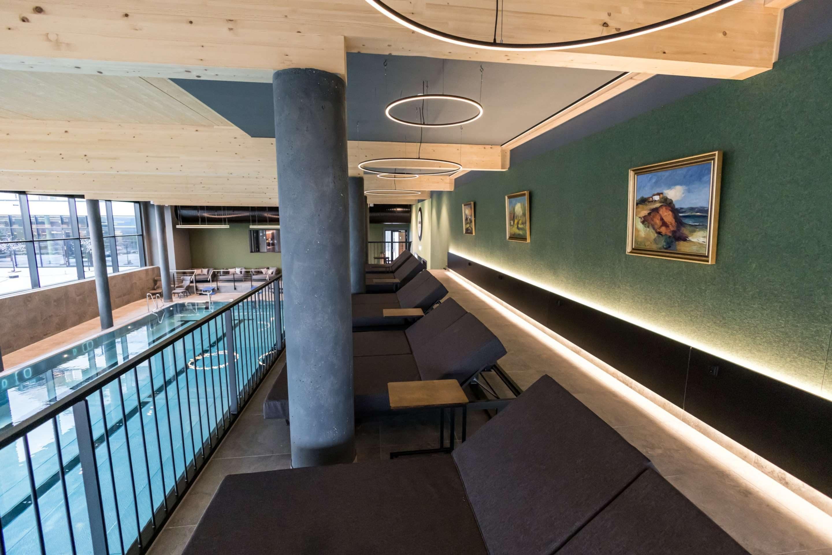 Un área de descanso moderna con asientos, barandilla de cristal con vista a una piscina y obras de arte en las paredes.