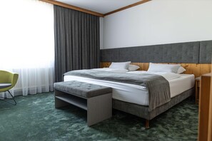 A hotel room with a bed, a bench, a chair, and a large window with curtains. - Gut Matheshof BW Signature Collection (Rieden)