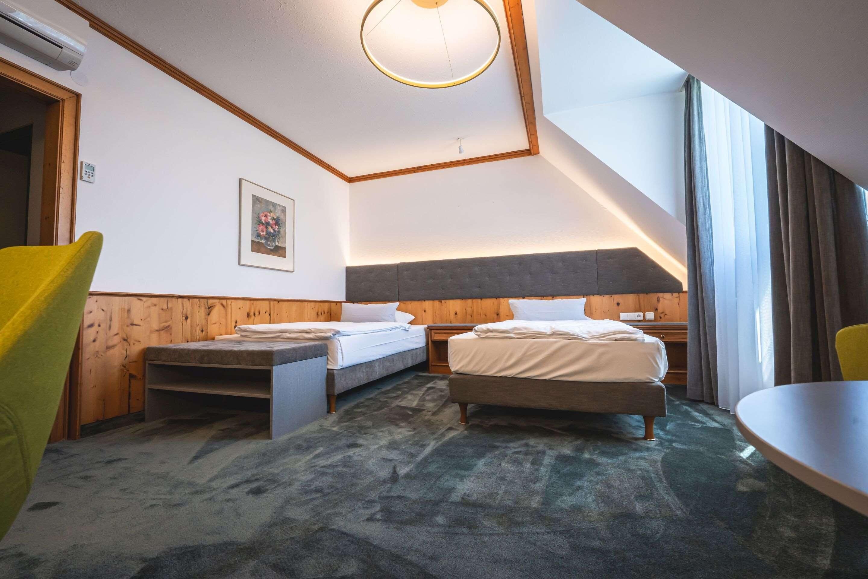 Habitación de hotel con dos camas, una mesa de comedor, una silla, una lámpara en el techo y un cuadro en la pared.