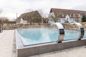 A swimming pool with a stone wall and metal railings, surrounded by buildings with traditional architecture. - Gut Matheshof BW Signature Collection (Rieden)