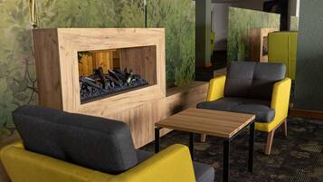 A modern lounge area with yellow and gray chairs, a wooden table, and a built-in fireplace.