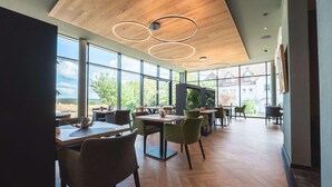 Un espace de restauration moderne doté de grandes fenêtres, d’un plafond en bois et de luminaires circulaires.