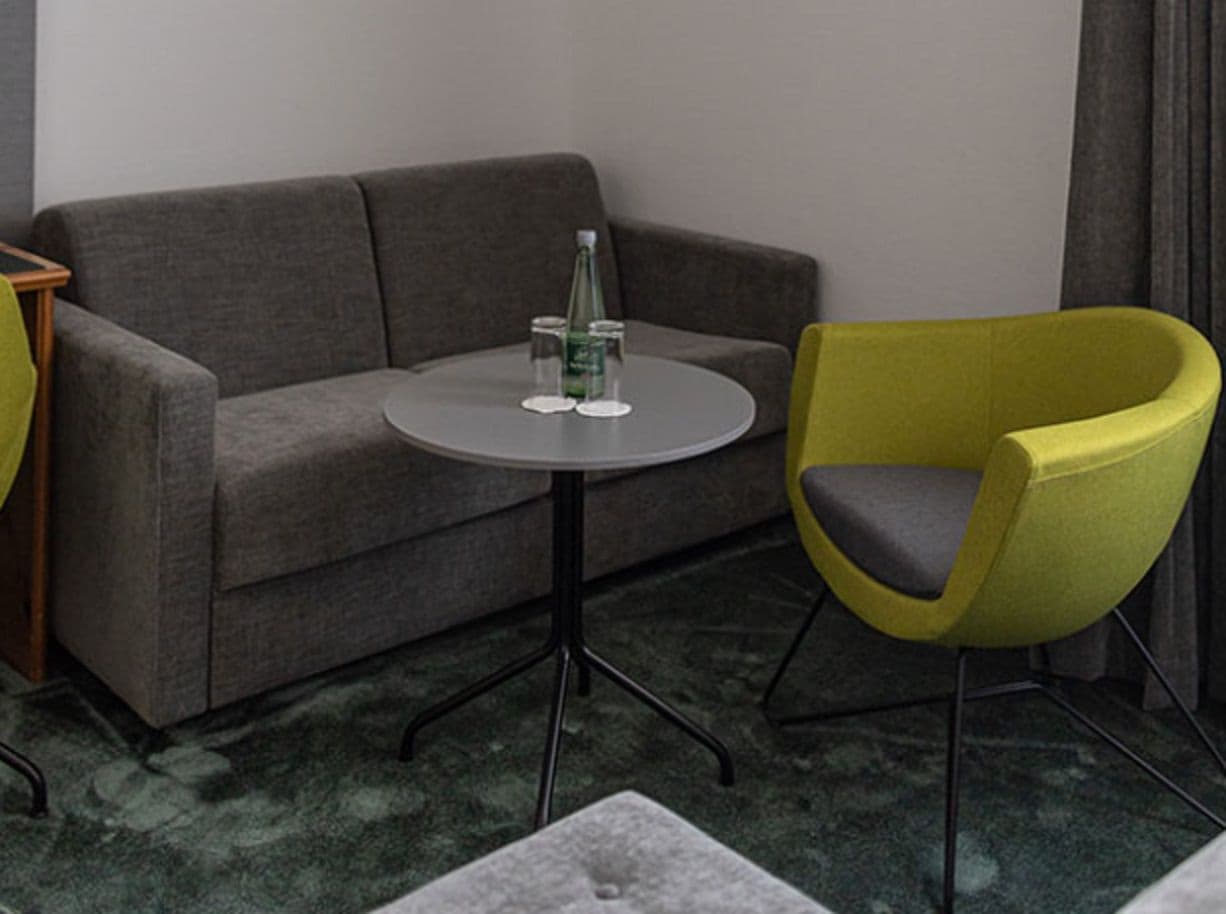 Una habitación con un sofá gris, una mesita redonda con una botella y una silla amarilla.