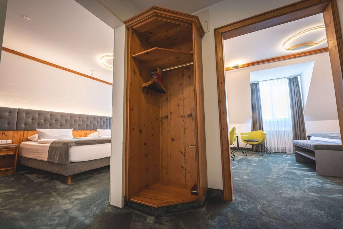 A hotel room with a bed, a wooden closet, a desk with a chair, and a sofa.