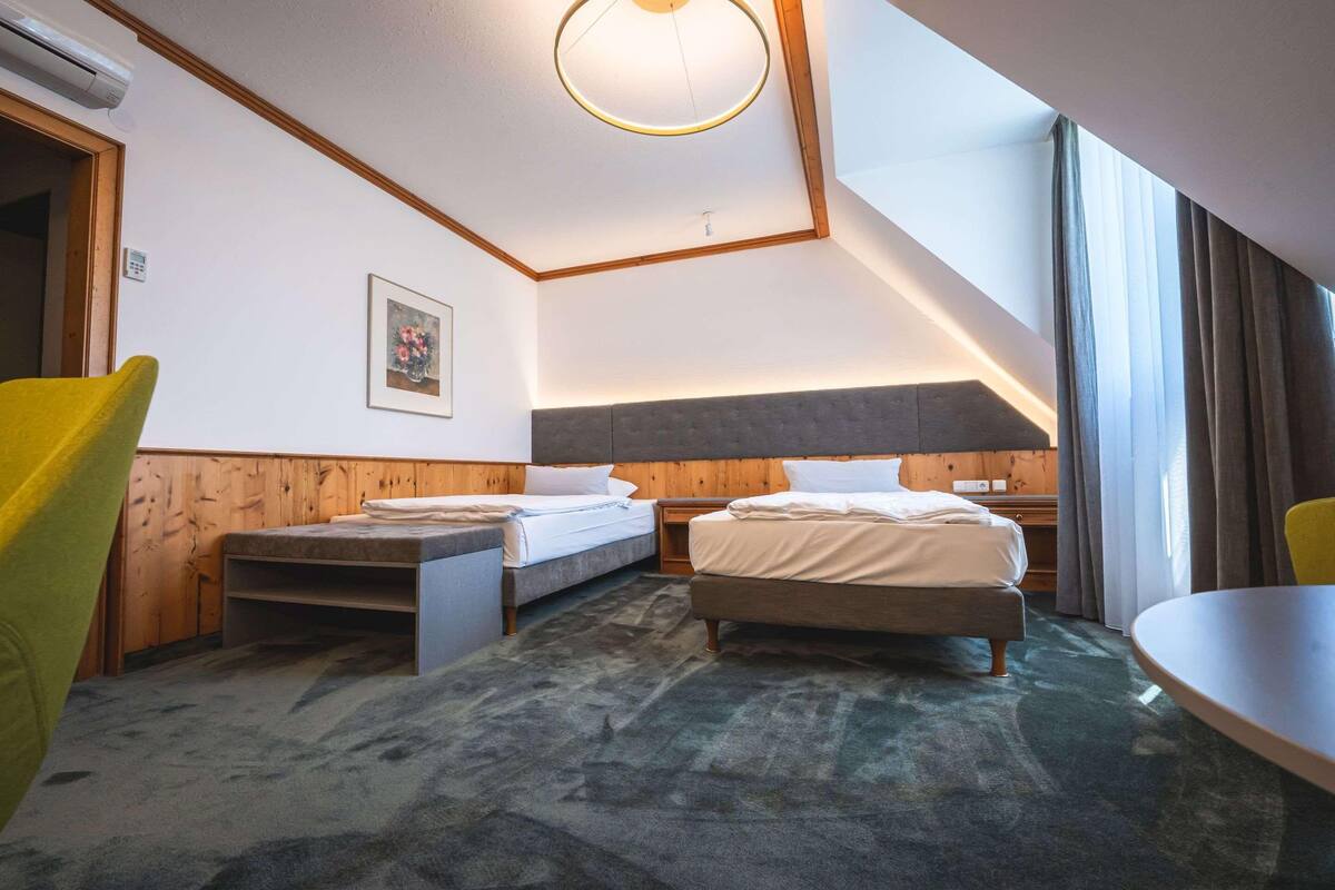 A hotel room with two beds, a dining table, a chair, a ceiling light fixture, and a framed picture on the wall.