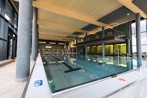 An indoor swimming pool with a glass barrier, wooden beams, and a mezzanine level. - Gut Matheshof BW Signature Collection (Rieden)