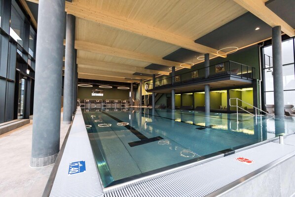 An indoor swimming pool with a glass barrier, wooden beams, and a mezzanine level. - Gut Matheshof BW Signature Collection (Rieden)