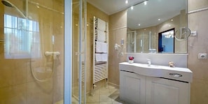 Un baño moderno con cabina de ducha de vidrio, tocador blanco con espejo y perchero.