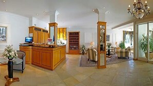 A spacious lobby with a wooden reception desk, seating area, and a large mirror. - Hotel Sacher Stoiber (Bad Fuessing)