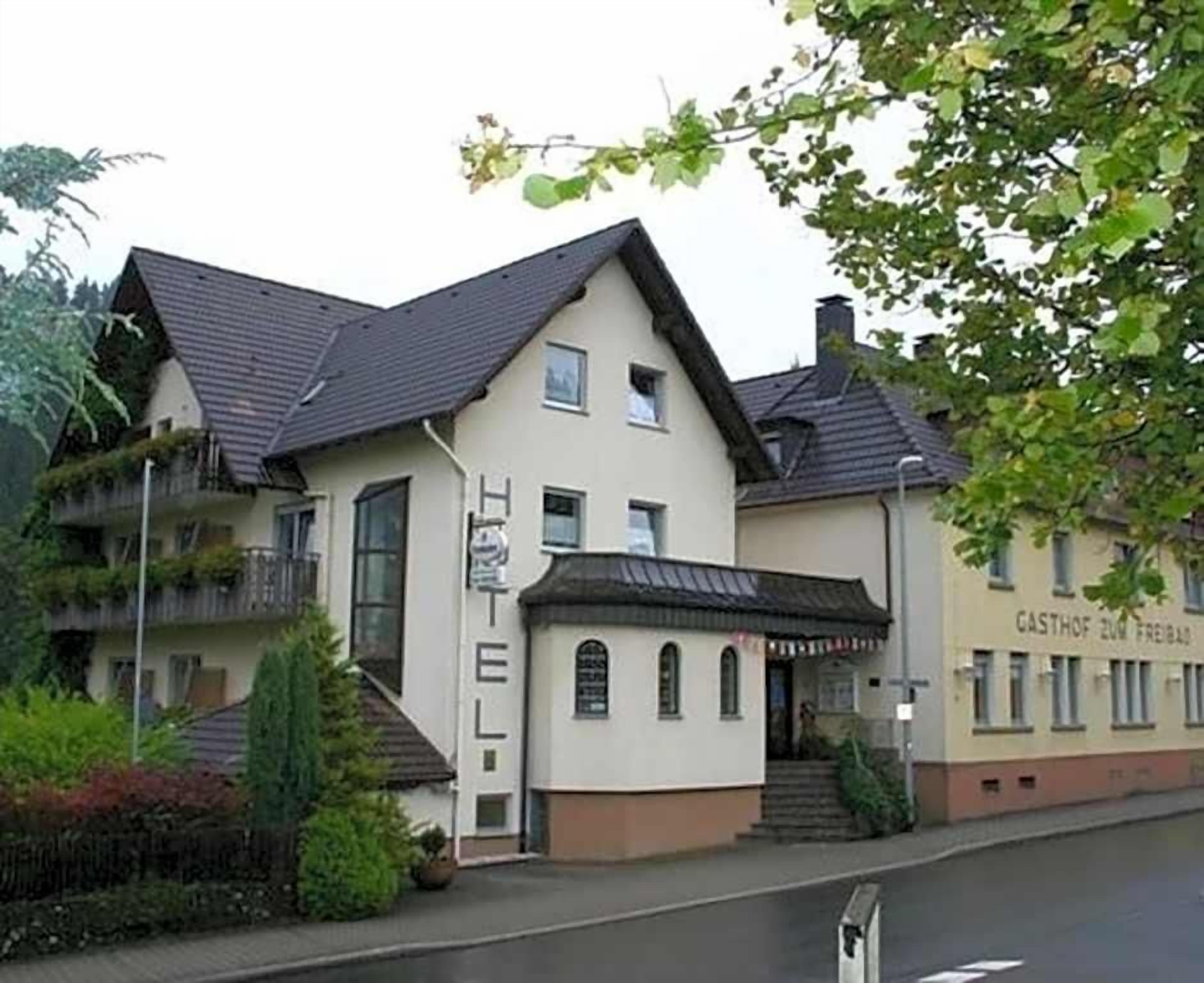 A two-story building with a flat roof, a balcony on the upper floor, and a small entrance with steps.