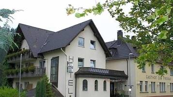 Een gebouw met twee verdiepingen, voorzien van een plat dak, een balkon op de bovenste verdieping en een kleine entree met treden.