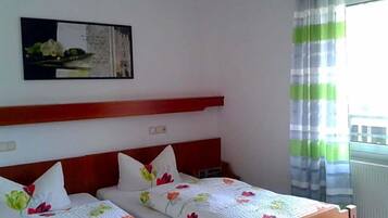 Een hotelkamer met twee bedden, een houten hoofdbord, een schilderij aan de muur en een raam met gordijnen.