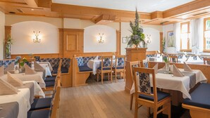 A restaurant with wooden booths and tables, blue cushioned seating, and floral centerpieces. - Zum Kirchenwirt (Neukirchen vorm Wald)