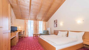 A bedroom with a wooden ceiling, a bed, a desk with a computer, a chair, and a window with curtains. - Zum Kirchenwirt (Neukirchen vorm Wald)