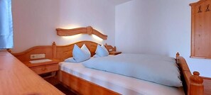 Un lit simple avec une tête de lit en bois, une table de chevet et une petite table à poser près du lit.