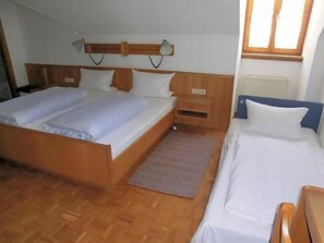 A bedroom with a double bed, a smaller bed, a nightstand, a lamp, and a window.
