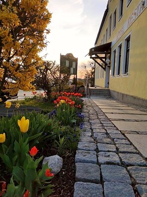 A hotel with a stone pathway leading to the entrance, surrounded by a flower bed with tulips and other plants.