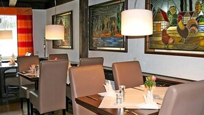 A restaurant interior with wooden tables, cushioned chairs, and framed artwork on the walls. - Hotel Zum Wersehof (Ahlen)