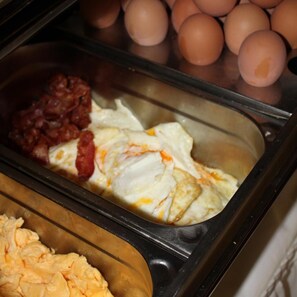A breakfast buffet with scrambled eggs, bacon, and eggs in a glass container. - Hotel Zum Wersehof (Ahlen)