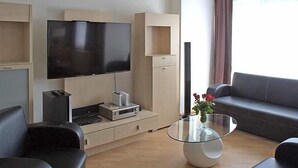 A modern living room with a flat-screen TV, a glass coffee table, a sofa, and a TV stand with electronic devices. - Hotel Zum Wersehof (Ahlen)