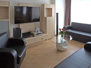 A modern living room with a flat-screen TV, a glass coffee table, a sofa, and a TV stand with electronic devices.