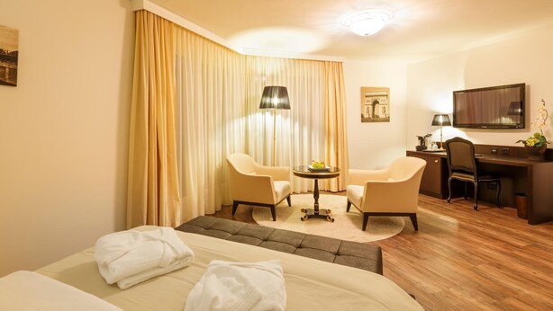 A hotel room with a bed, two armchairs, a desk, and a television. - Business Hotel First (Feusisberg)