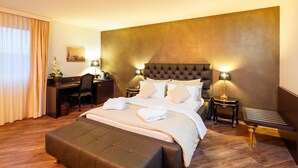A hotel room with a large bed, a desk, and a chair. - Business Hotel First (Feusisberg)