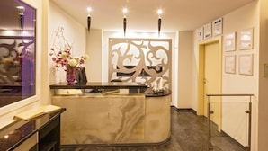 Un comptoir d’accueil avec un plateau en marbre, un vase rempli de fleurs et un panneau décoratif orné de motifs découpés.