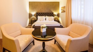 A hotel room with a bed, two armchairs, a round table, and a nightstand with lamps. - Business Hotel First (Feusisberg)