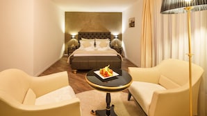 Une chambre d’hôtel avec un lit, deux fauteuils, une petite table avec des fruits et une lampe sur pied.