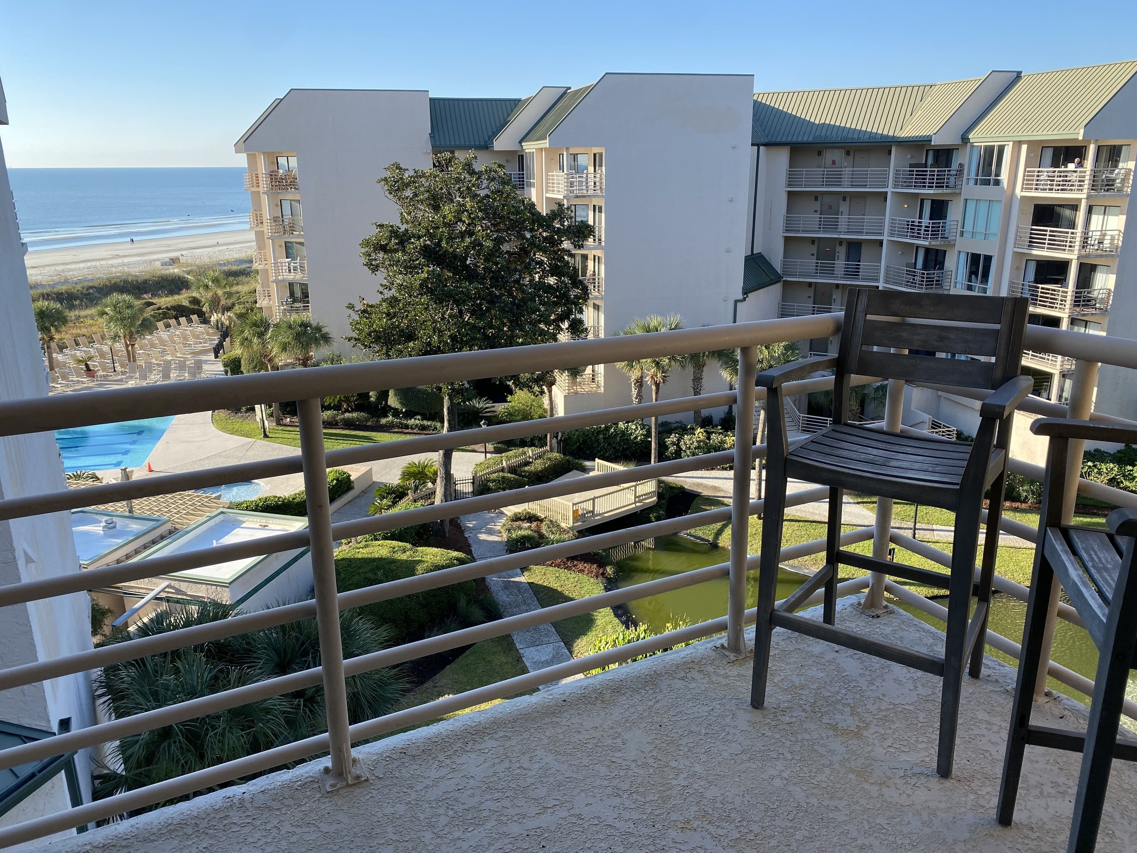 Un balcón con vista a la playa, una piscina y edificios cercanos.