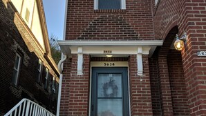 A two-story brick building with a black front door, white railings, and a small window above the door. - Lovely, cozy Beacon guest suite with portable kitchen in Squirrel Hill (Pittsburgh)