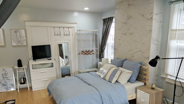 A bedroom with a bed, bedside tables, a TV, a wardrobe, and a window with curtains. - Lovely, cozy Beacon guest suite with portable kitchen in Squirrel Hill (Pittsburgh)