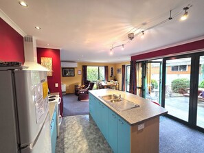 A modern kitchen with a central island, a dining area with chairs, and a view through large sliding doors to an outdoor space. - Popular Family friendly, Modern Cosy Bach,+ WiFi, 21 Devon Street Hanmer Springs (Hanmer Springs)
